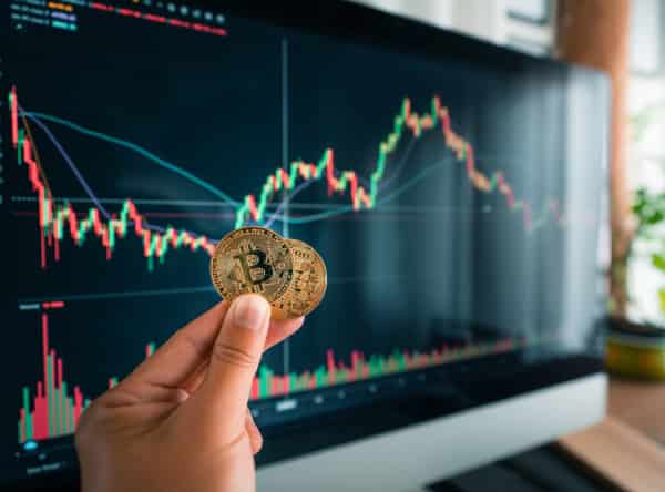 Main tenant Bitcoin devant graphique boursier